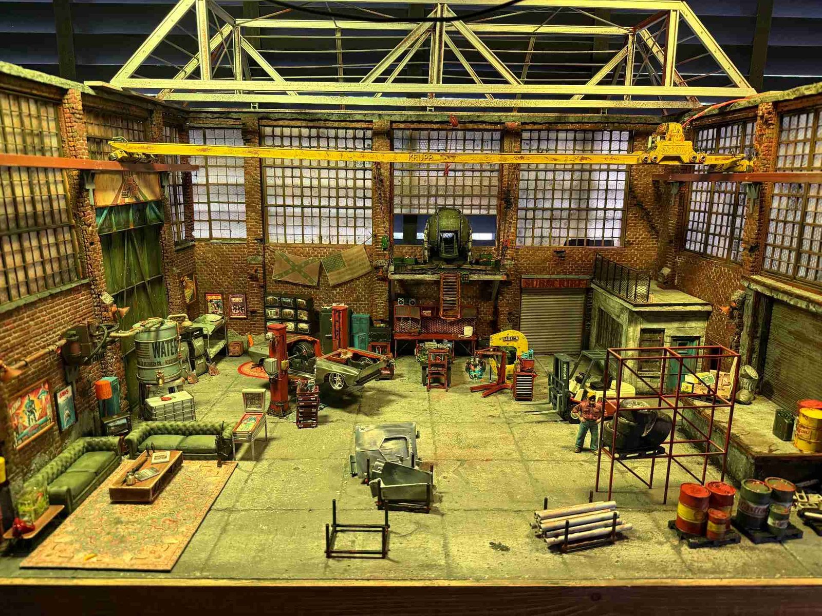 Complete interior view of Mad Max 1:24 scale diorama garage with rusty crane, brick walls, miniature classic cars, and industrial clutter