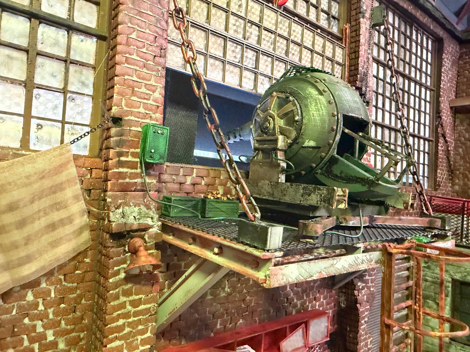 Upper mezzanine level of 1:24 Mad Max garage diorama featuring a rusted industrial motor suspended by chains above brick walls