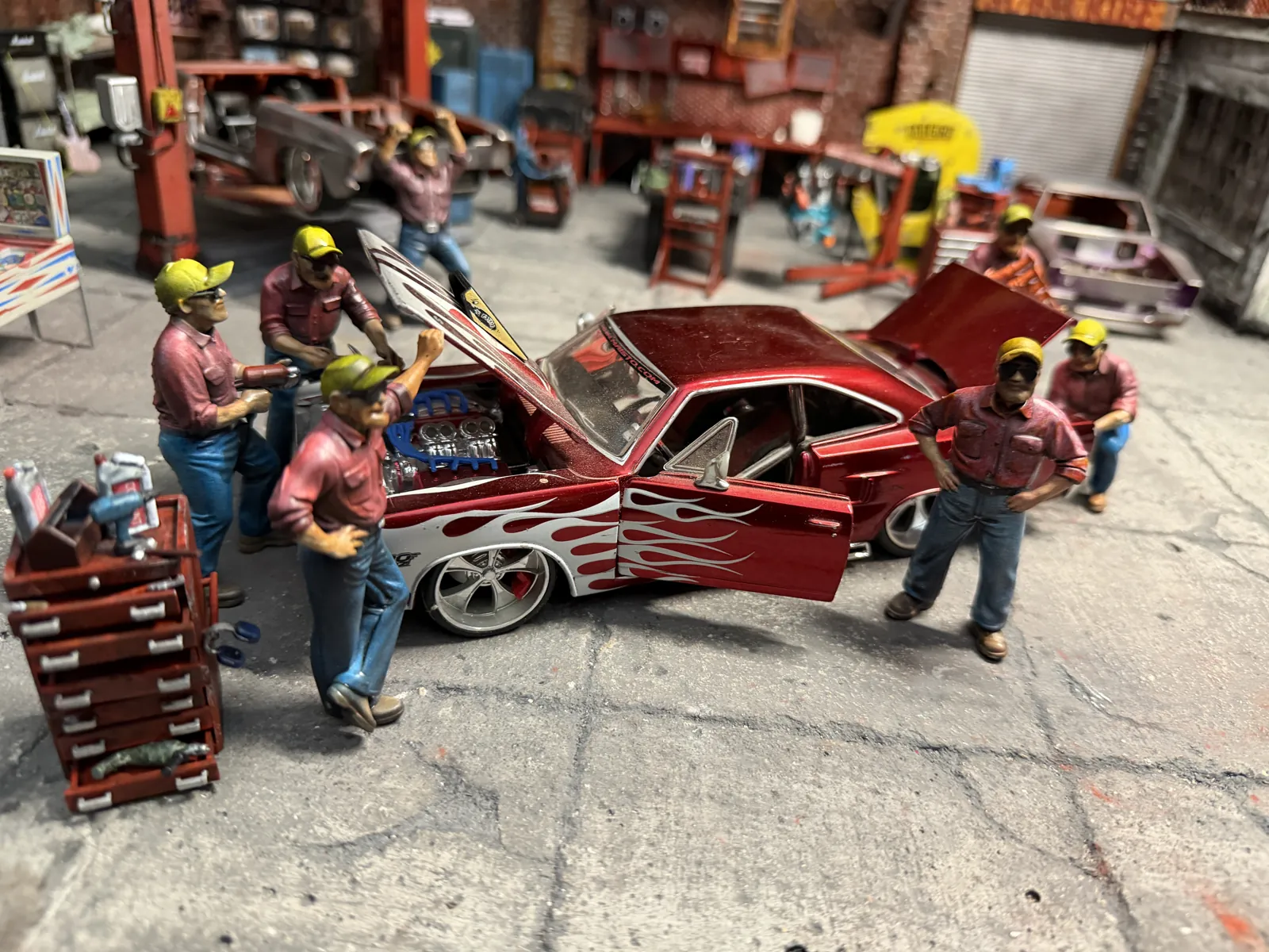 Mechanic figures working on a flamed red muscle car inside the 1:24 garage diorama